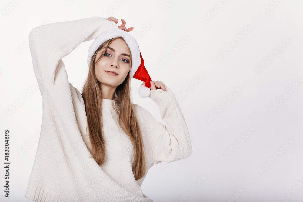 Portrait of smiling blond woman in Santa Claus Hat. Pretty young model with blonde long hair, wide eyebrows and blue eyes posing on camera in studio. isolated. Portrait of smiling blond woman in Santa Claus Hat. Pretty young model with blonde long hair, wide eyebrows and blue eyes posing on camera in studio. isolated.