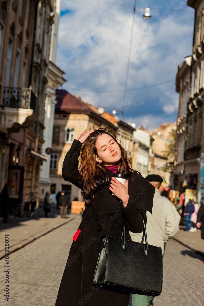 Brunette woman with long hair posing with coffee in the hands of the street