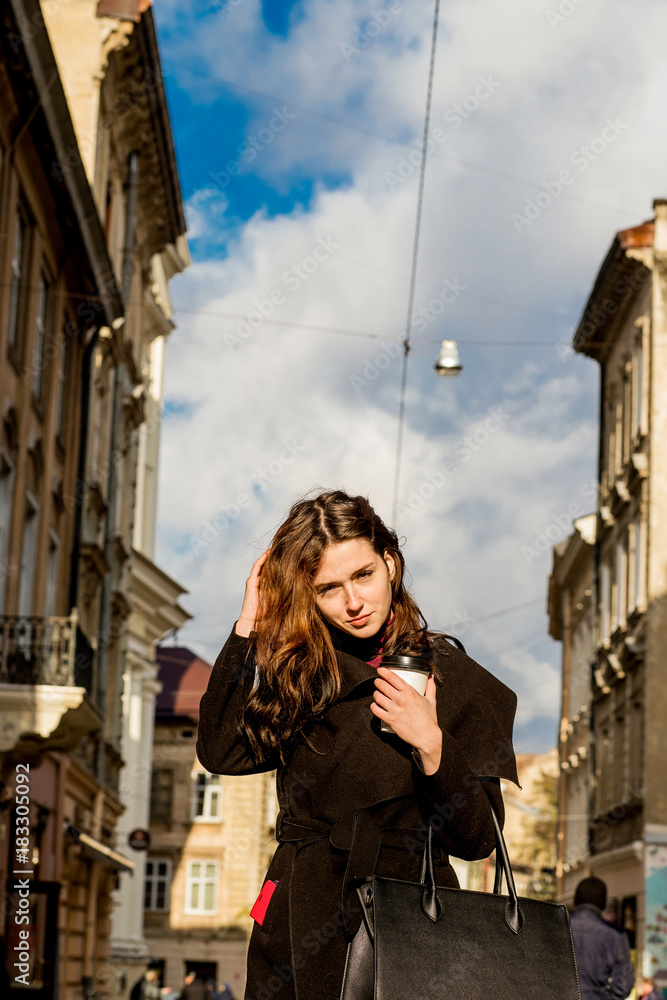 Brunette woman with long hair posing with coffee in the hands of the street