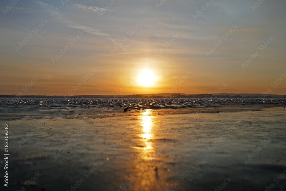 The frozen lake meets with the bent sunset. Verkh-Isetskoe reservoir, Ekaterinburg, Sverdlovsk oblast, Russia. The frozen lake meets with the bent sunset. Verkh-Isetskoe reservoir, Ekaterinburg, Sverdlovsk oblast, Russia.