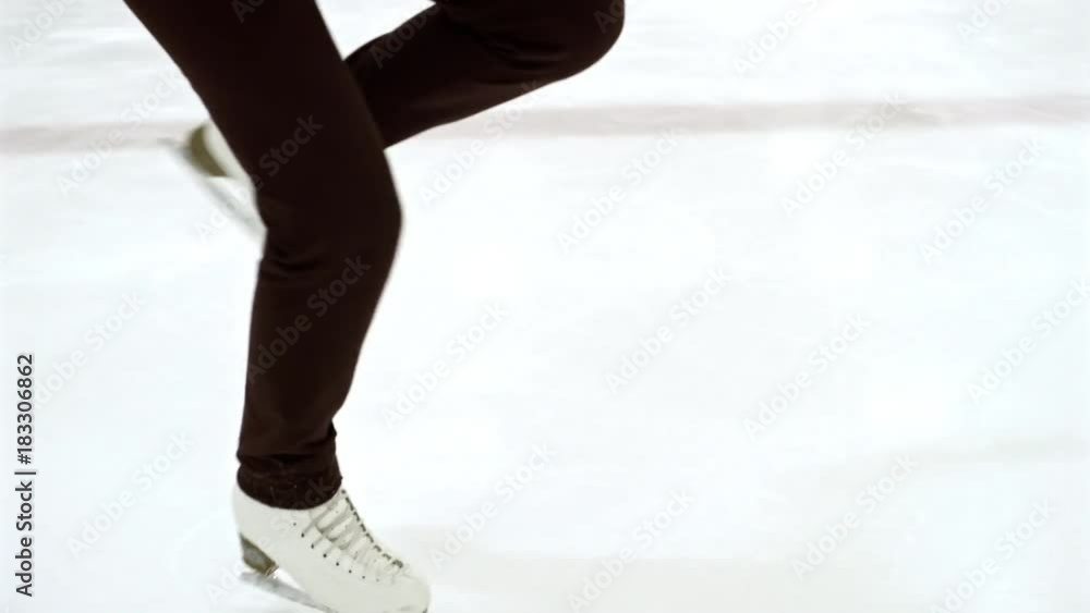 Handheld camera shot from legs up to face of professional female figure skater spinning on indoor ice rink
