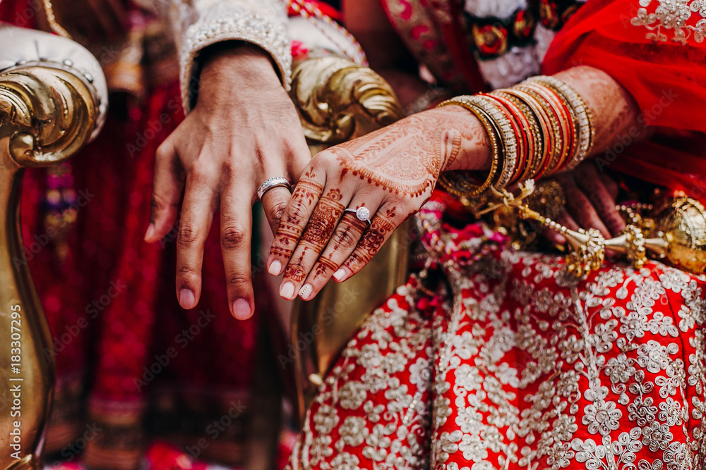 Tender hands of an Indian bride covered with henna tattoo and groom's arm side by side with wedding rings