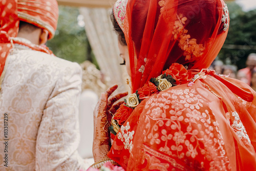 Look from behind at stunning Indian bride dressed in red lehenga and veil photo