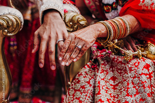 Tender hands of an Indian bride covered with henna tattoo and groom's arm side by side with wedding rings