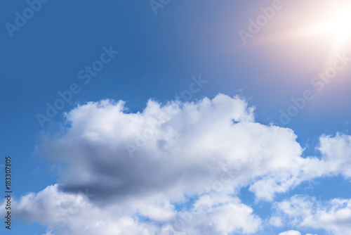 fluffy clouds in bright blue sky with beams of sunlight background