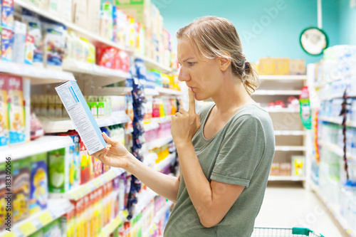 Young woman in supermarket groceries carefully reading nutrients of cornflakes quick breakfast. Healthy eating concept