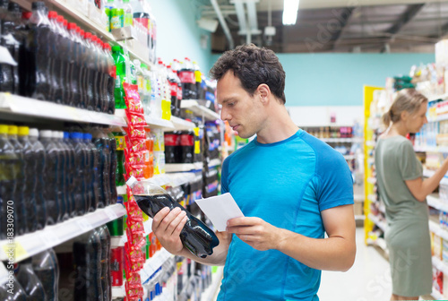 Handsome caucasian man shopping in a supermarket. Man carefully reading nutrients of bottle with beverage