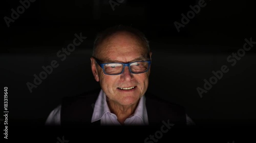 4k video 73 years old happy senior man sitting in front oh hise computer talking via skype at home in the evening
 photo