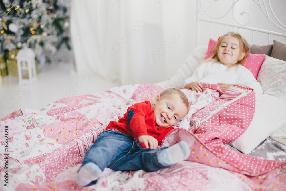Happy cute children posing near Christmas tree in a holiday interior. Little brother and sister in a cozy Christmas room