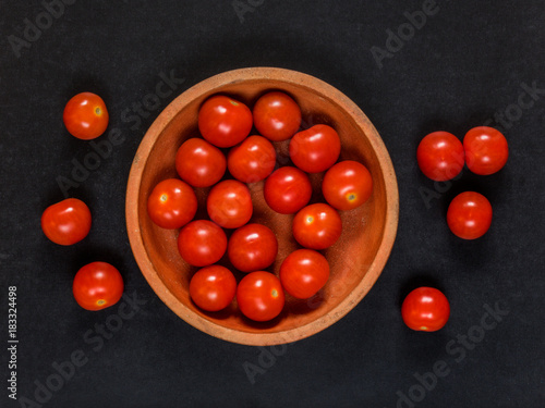 Clay dish with cherry tomatoes on black background