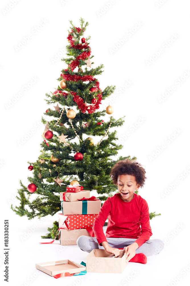 Portrait of cute mixed race little boy unpacking gifts near Christmas tree and taking digital tablet out of box