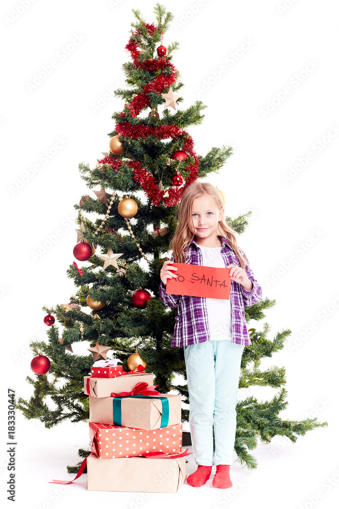 Portrait of little girl standing near Christmas tree with letter to Santa in her hands on white background