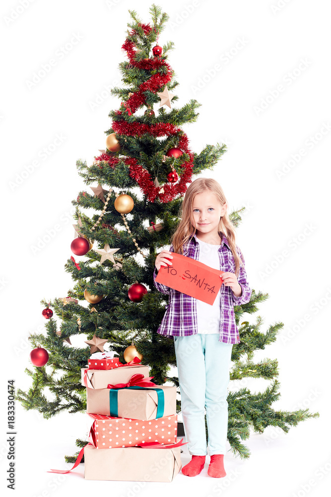 Portrait of little girl standing near Christmas tree with letter to Santa in her hands on white background