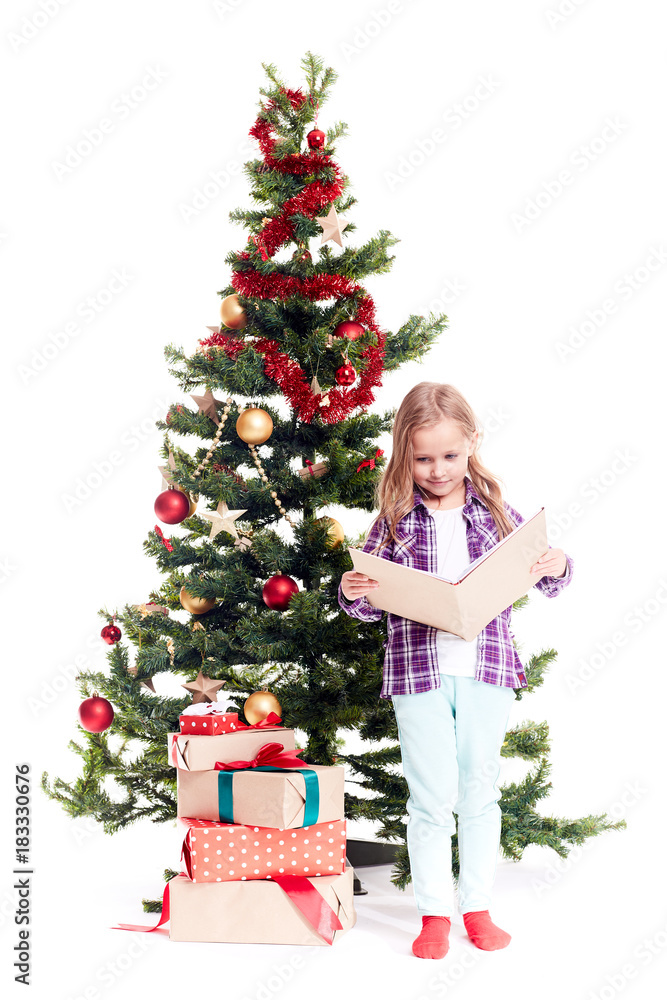 Portrait of cute little girl reading book near Christmas tree on white background Portrait of cute little girl reading book near Christmas tree on white background