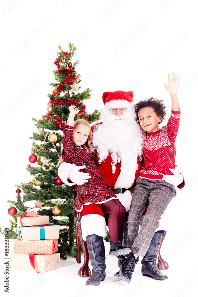 Santa Claus sitting in chair near Christmas tree with multi-ethnic boy and girl on his lap Santa Claus sitting in chair near Christmas tree with multi-ethnic boy and girl on his lap