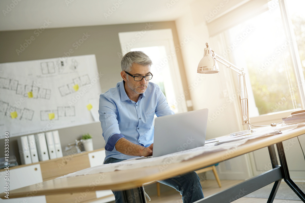 © goodluz - Architect in office working on construction project using laptop
