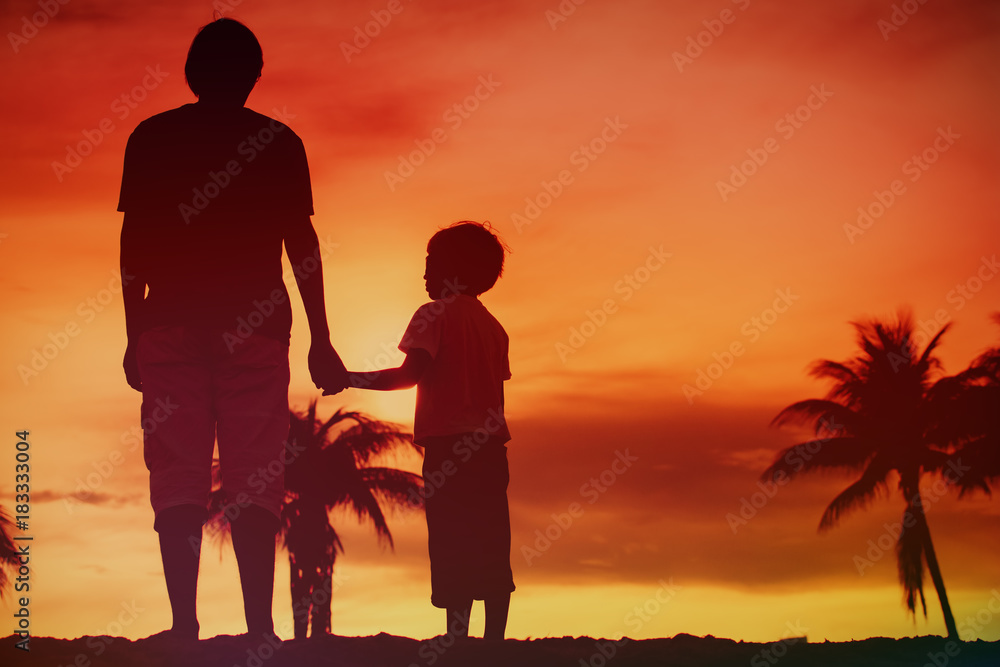 silhouette of father and son holding hands at sunset beach