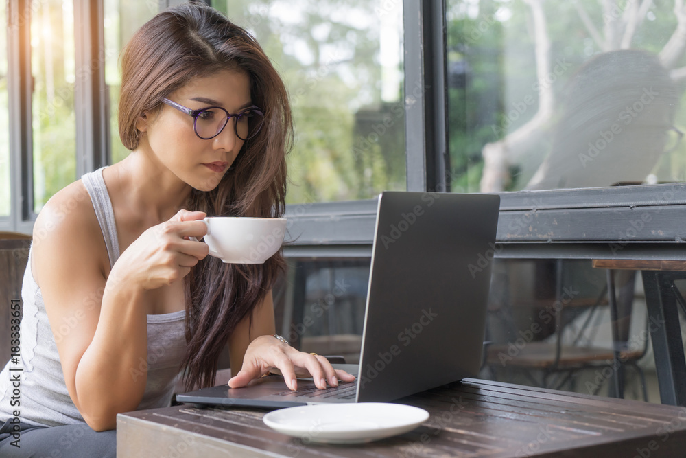 Casual business woman working on laptop. Young girl using computer outdoor drinking coffee in cafe.