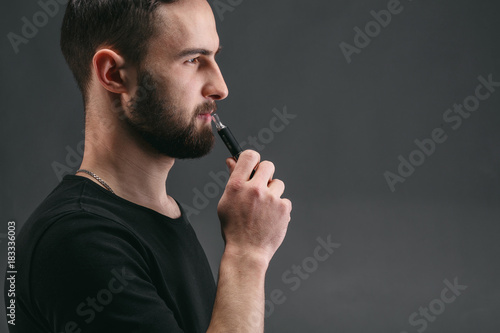 Young man vaping e-cigarette with smoke on black