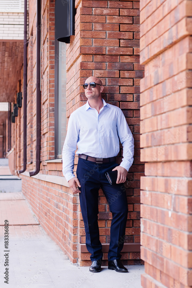 businessman full height outdoor staing at red brick building. shirt dark blue trousers, boots