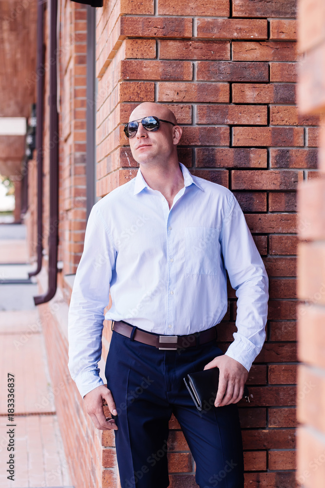 bald businessman staing at red brick wall building. shirt dark blue trousers, sunglasses. outdoor spring, summer bald businessman staing at red brick wall building. shirt dark blue trousers, sunglasses. outdoor spring, summer