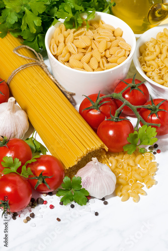 spaghetti, tomatoes and fresh ingredients on a white table, vertical top view
