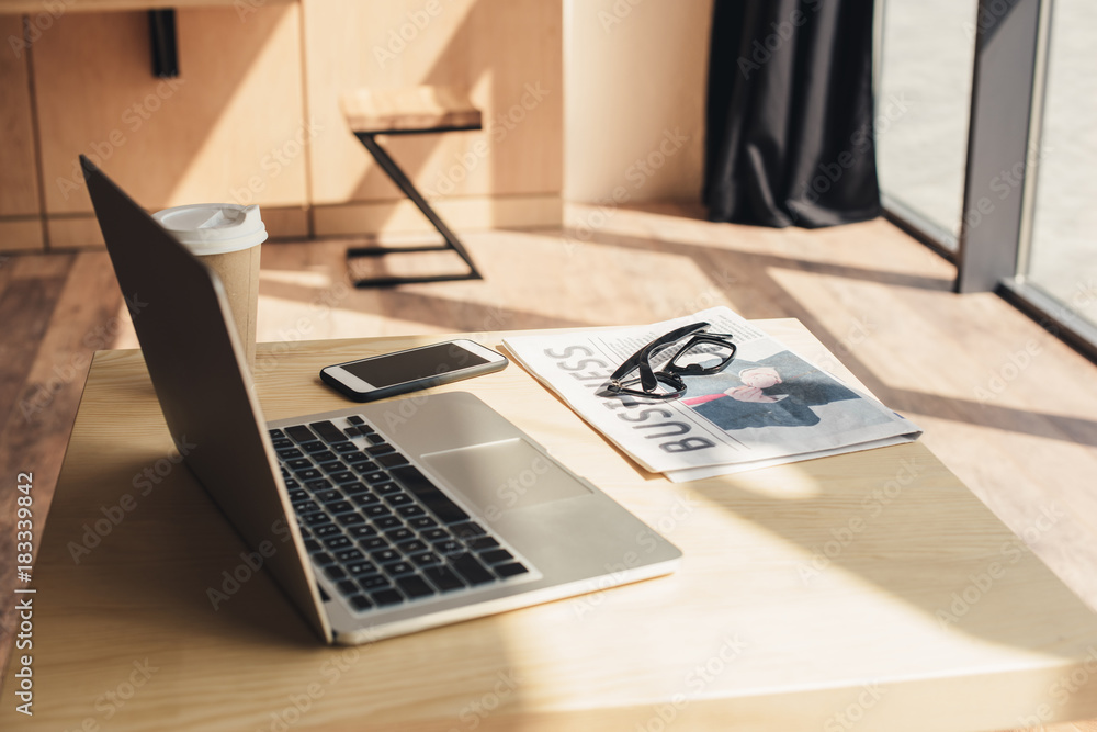 laptop, smartphone, eyeglasses and business newspaper on table in coffee shop laptop, smartphone, eyeglasses and business newspaper on table in coffee shop
