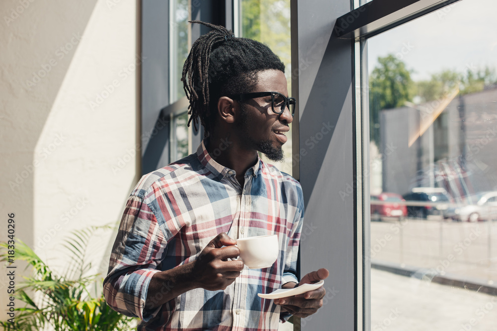african american man drinking coffee while standing at window