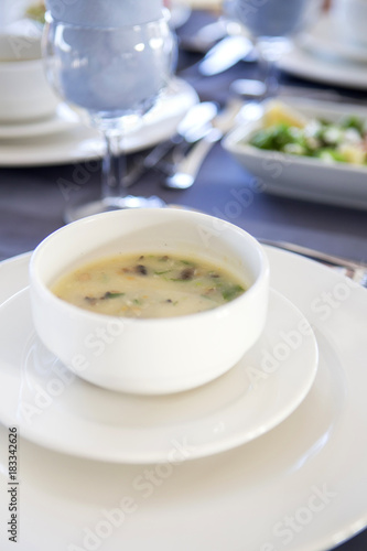 Delicious seafood meal soup with fish and vegetables on a plate in the restaurant. Spoons, forks and knives on the table, all prepared for celebration evening. Dim sunset light, outdoors