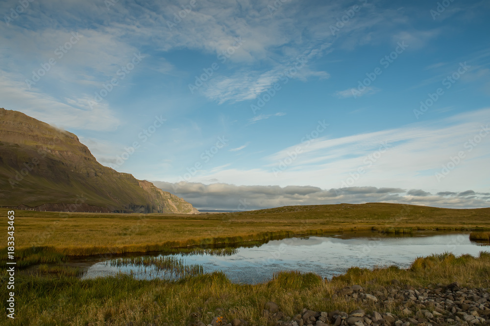 A small lake against a background of green hilly mountains. Traditional landscape of Iceland. Beautiful northern landscape.

