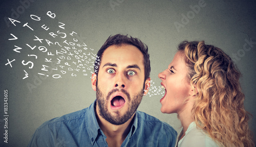 Angry woman screaming something in the ear of a shocked, scared guy isolated on gray wall background. photo