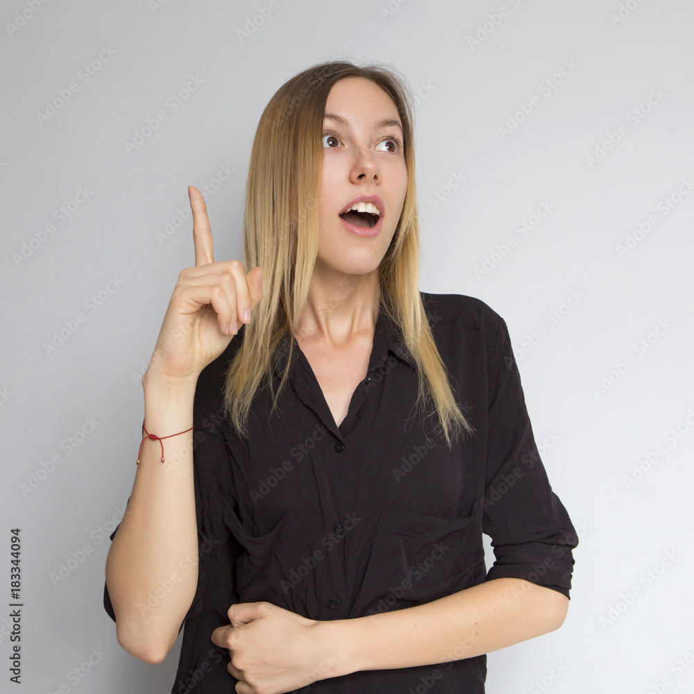 Beautiful brunette caucasian woman in dark black blouse with bright emotions standing on a neutral grey background. Her hands make a gesture. She smiling Beautiful brunette caucasian woman in dark black blouse with bright emotions standing on a neutral grey background. Her hands make a gesture. She smiling