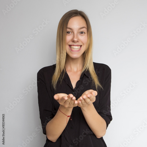 Beautiful brunette caucasian woman in dark black blouse with bright emotions standing on a neutral grey background. Her hands opened in a gesture. She smiling