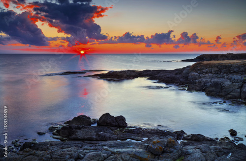 Beautiful sunrise on rocky shore and dramatic sky clouds