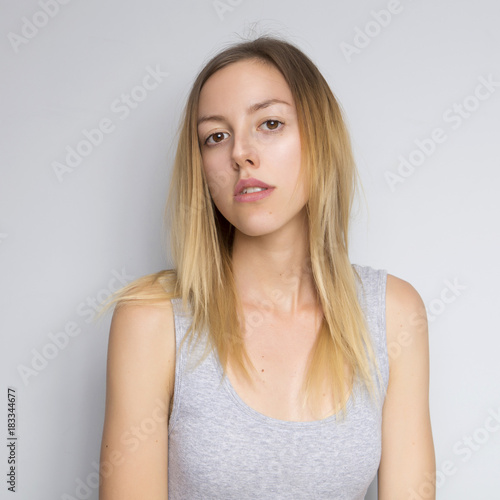 Beautiful brunette caucasian woman in grey blouse with bright emotions standing on a neutral grey background. Her hands make a gesture. She act sexy, seductive