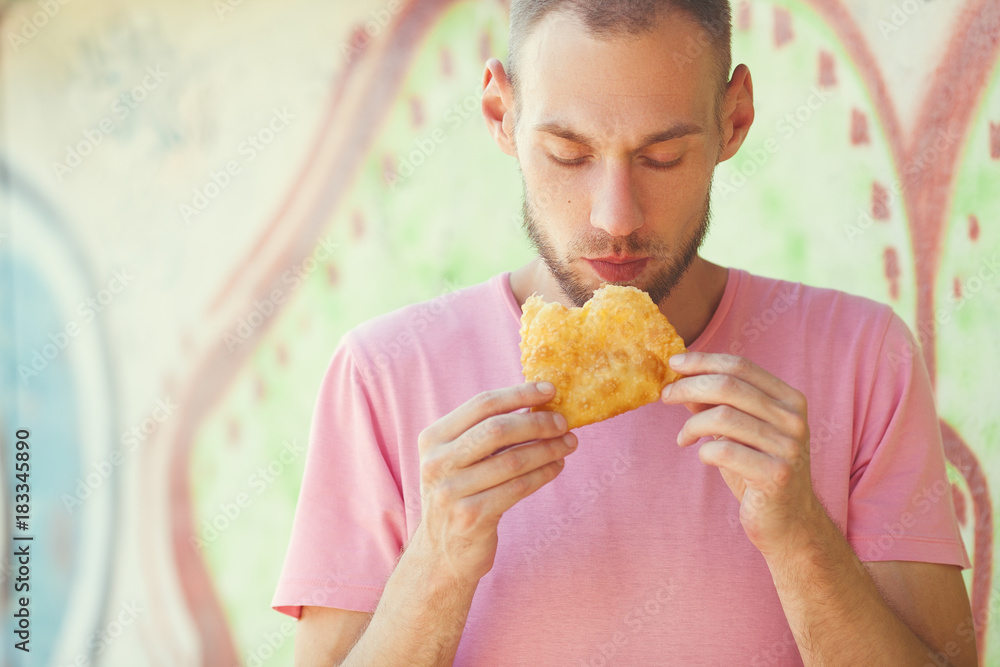 Street food concept. Young handsome hipster guy holding, eating meat pasty. Traditional dish of Turkic, Caucasian, Mongolian cuisines. Close up. Text-space. Outdoor shot Street food concept. Young handsome hipster guy holding, eating meat pasty. Traditional dish of Turkic, Caucasian, Mongolian cuisines. Close up. Text-space. Outdoor shot
