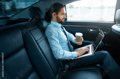 Man Working On Notebook And Drinking Coffee in Car. © puhhha