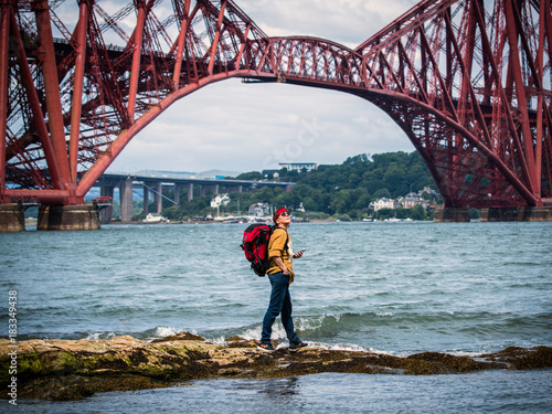 Concept travel. Active middle-aged woman with a backpack and mobile phone  standing under the Forth Railway Bridge Edinburgh  looking up.