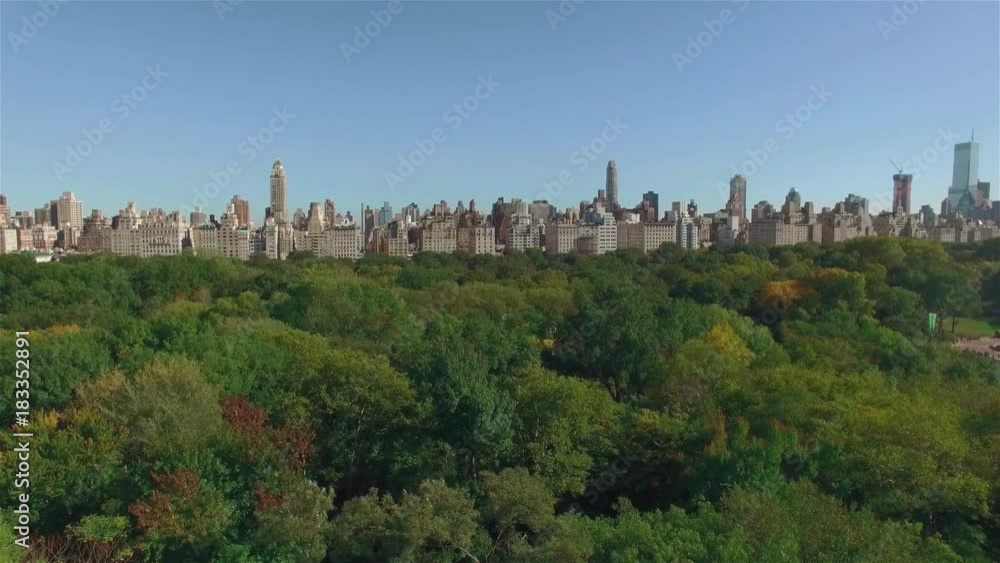 Aerial shot of New York Central Park, camera moving slowly to the left over it, city view behind the trees. Concept of a green zone in a city. Aerial shot of New York Central Park, camera moving slowly to the left over it, city view behind the trees. Concept of a green zone in a city.