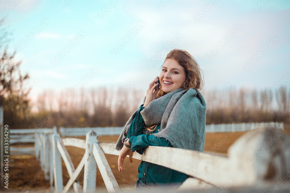 Cheerful blonde woman talking on phone outside on autumn field.