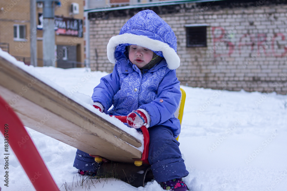 little girl swinging on a swing in a playground on a winter day - obrazy, fototapety, plakaty 