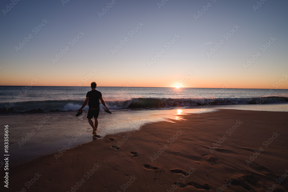 Man walking on the beach with shoes in his hands in Portugal