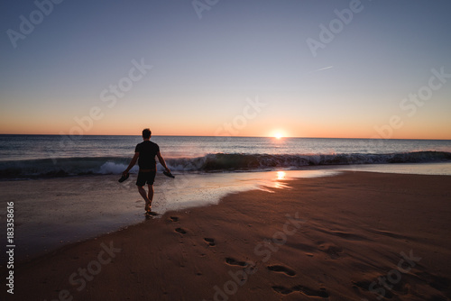 Man walking on the beach with shoes in his hands in Portugal