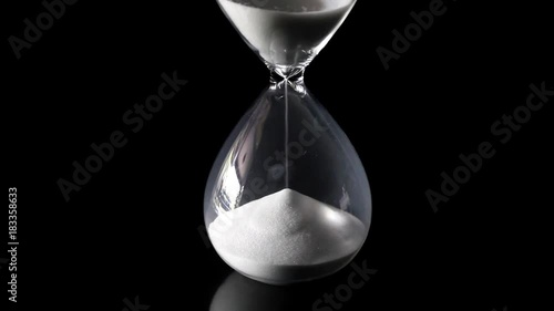 Falling sand showing the passing time of hourglass close-up and isolated on glossy black floor and background. Presented in the centre of the screen. photo