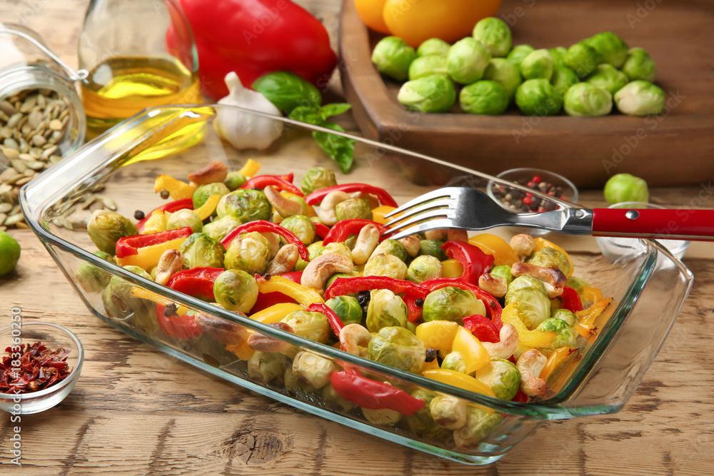 Glass dish with baked Brussels sprouts, pepper and nuts on table Glass dish with baked Brussels sprouts, pepper and nuts on table