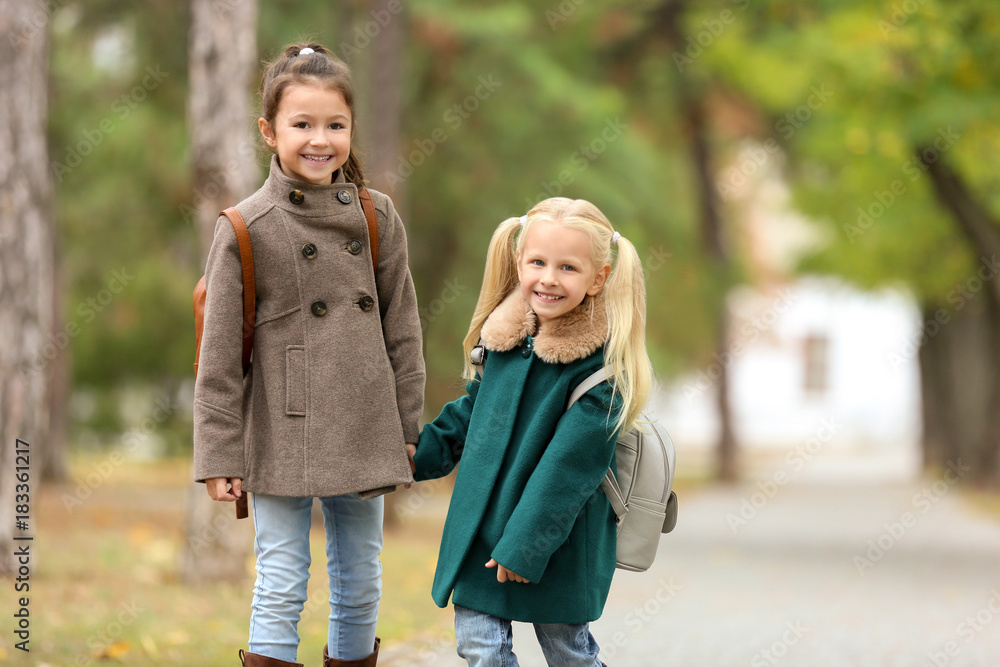 Cute little girls in outwear walking together in park