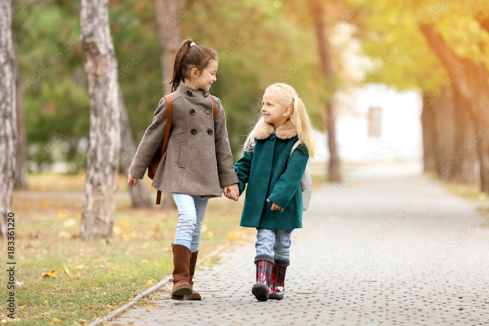 Cute little girls in outwear walking together in park Cute little girls in outwear walking together in park