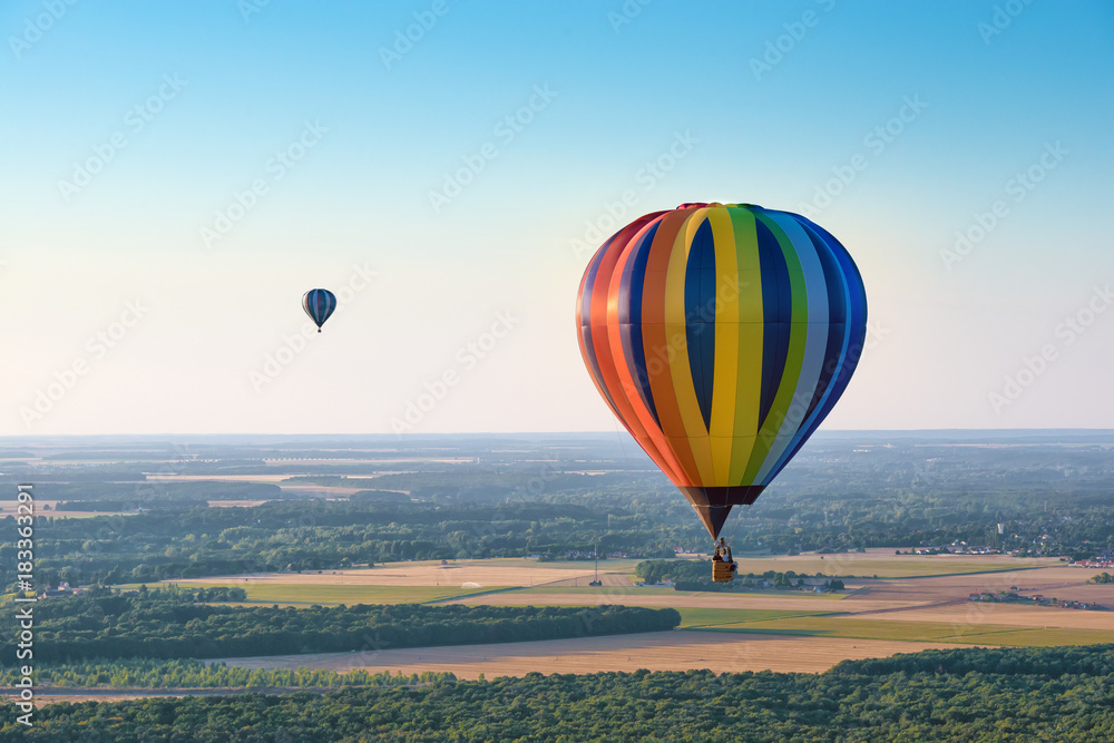 Naklejka premium Aerial view of multicolored hot air balloons flying over a forest on evening lighting
