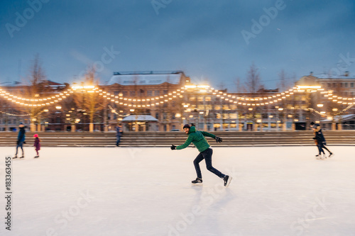 Outdoor portrait of active sporty bearded male involved in winter sport activities, prepares for skating competitions on Christmas ice ring decorated with garlands. Active lifestyle concept.