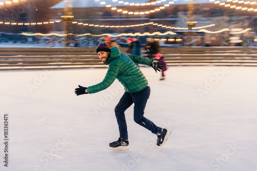 Male in speed demonstrates his skills of skating, has fun on ring, feels sure and confident on ice, spends free time outdoor, enjoys winter vacations, being photographed in movement